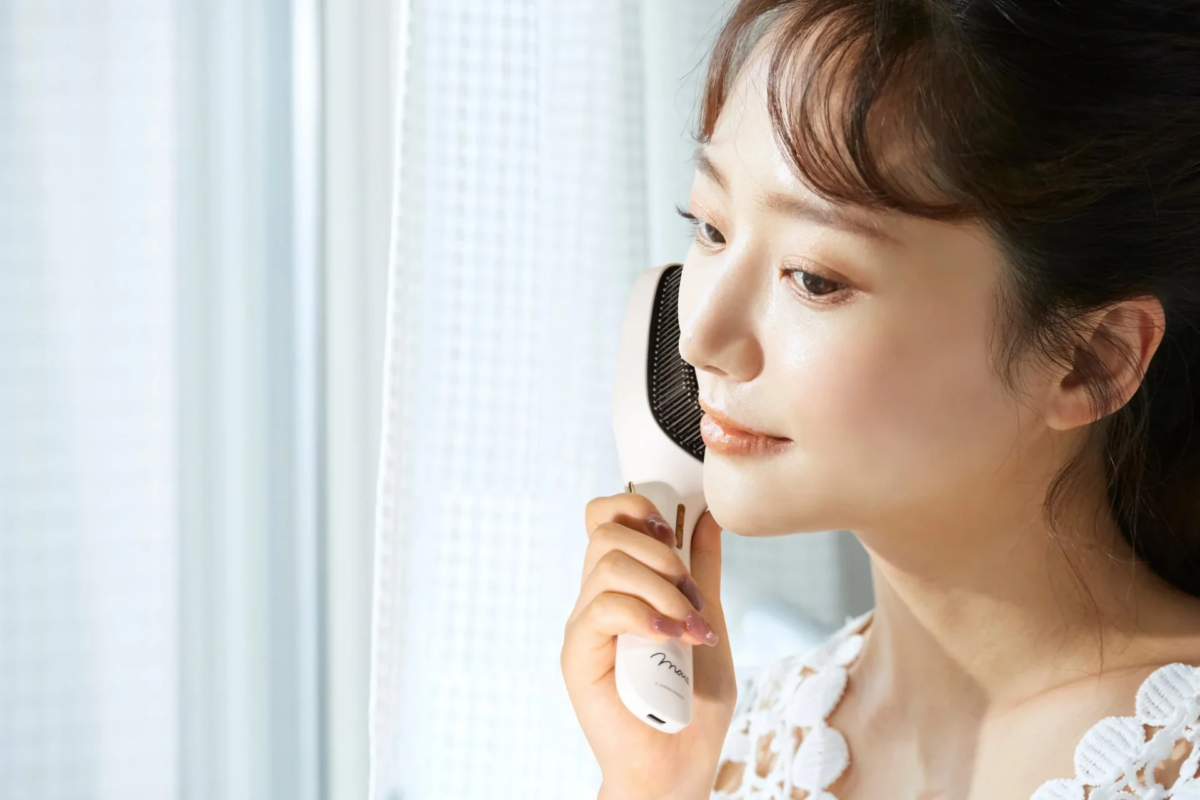 Mujer joven usando un dispositivo de belleza facial cerca de una ventana