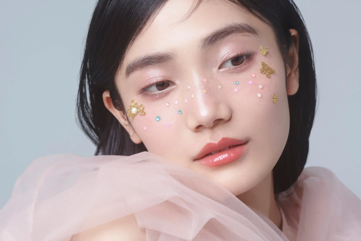 Primer plano de una mujer joven con maquillaje rosa y decoraciones faciales de mariposas y flores