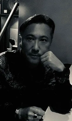 Retrato en blanco y negro de un hombre con camisa estampada, con la mano en la barbilla y expresión seria.