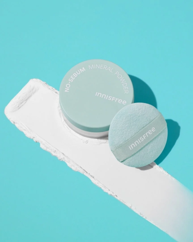El No-Sebum Mineral Powder de Innisfree con su borla sobre un fondo azul con polvo blanco.