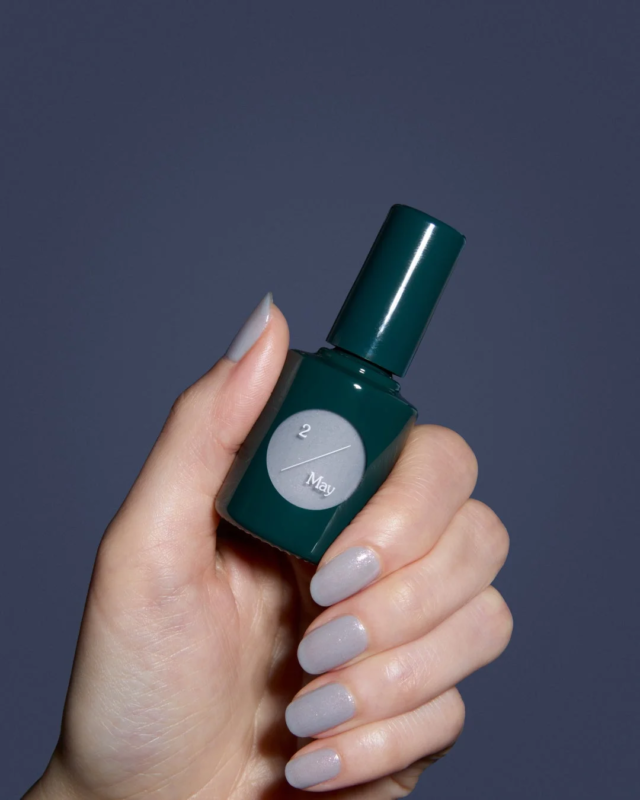 Mano con esmalte de u&ntilde;as y botella de uka Moon study