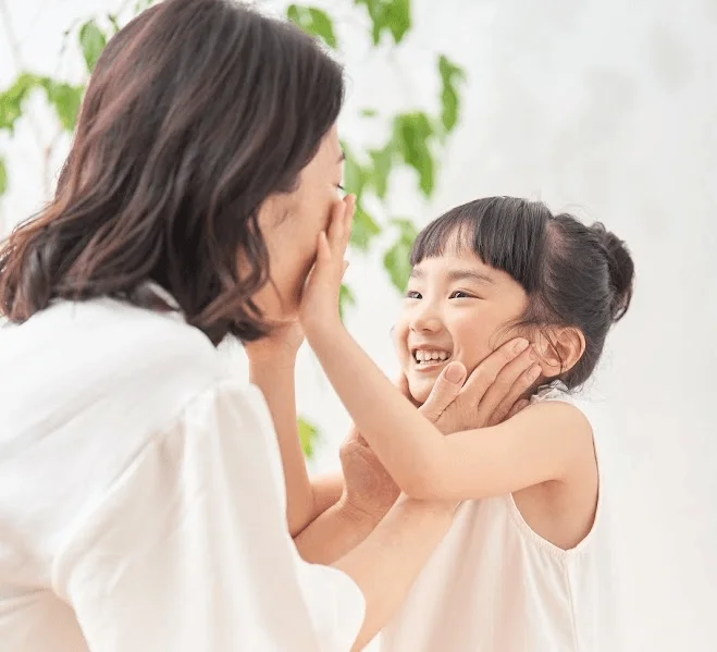 Madre e hija sonriendo y tocándose las mejillas